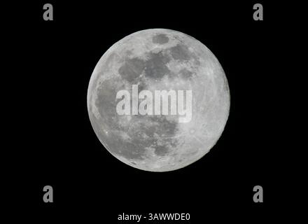 A detailed full moon captured with a telephoto lens, showing craters and surface textures against a black night sky. High contrast and sharp focus. Stock Photo