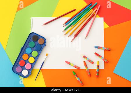 Crayons, colorful pencils, water color and pastel paint with drawing book on colorful paperboard, school painting concept Stock Photo