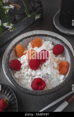 An easy healthy breakfast. A bowl filled with grainy, creamy cottage cheese is decorated with bright yellow and red raspberries. The dish stands on a Stock Photo