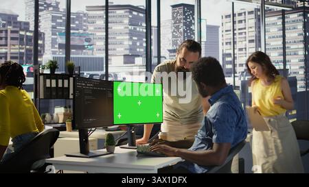 System administrator does software debugging on isolated screen PC, asking for help from coworker. Zoom in on admin fixing coding mistakes on chroma key computer, being assisted by colleague, camera B Stock Photo