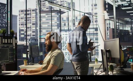 Managers evaluating work done by computer scientists in workspace doing software debugging. Management executives walking in office with tablet, checking code fixed by employees, camera B Stock Photo