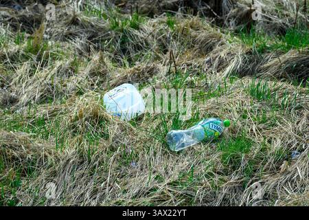 Empty plastic bottles discarded on the grass reveal the problem of littering in urban landscapes. The image shows a mix of green grass and brown dried Stock Photo