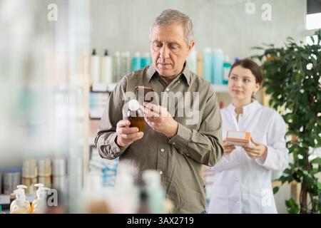 Mature man scans QR code on box cough syrup label. Female pharmacist offers various cough syrups Stock Photo