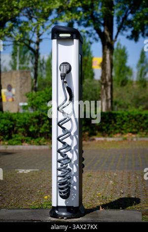 White charging station with slightly damaged charging cable in an empty parking lot against a blurred background Stock Photo
