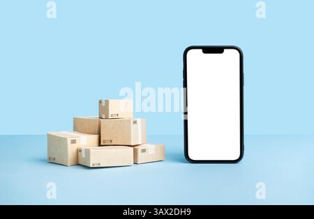 smartphone mockup with a blank screen next to stacked delivery boxes on a blue background. Stock Photo