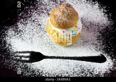 Cream puffs on a black plate sprinkled with icing sugar with a fork print Stock Photo