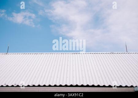 A modern corrugated white metal roof contrasts with a pale blue sky and soft clouds, creating a minimalist composition. Stock Photo