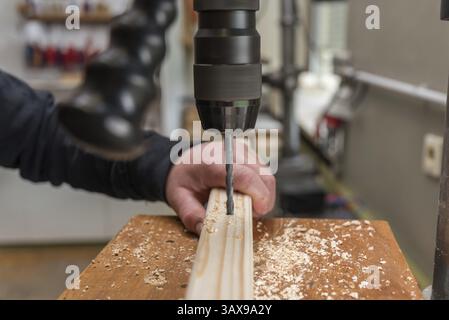 Carpenter drills a hole in the wood with an electric drill - close-up Stock Photo