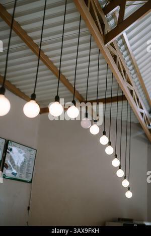 String of lights with bulbs hanging from a roof in a modern building. Decorative interior lighting with modern design. Stock Photo