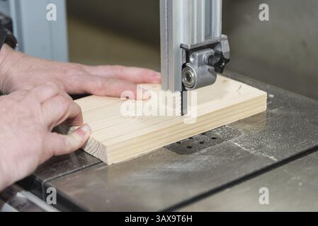 Carpenter saws softwood in wood workshop with band saw - Joinery Stock Photo