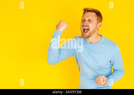 Excited man raising fists and shouting on yellow background Stock Photo