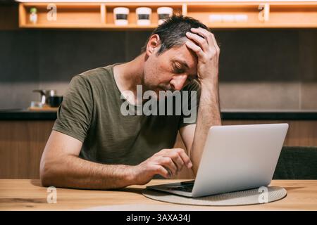 Tired exhausted freelancer working on a laptop computer late at night in home office, meeting the deadline for a remote job project, selective focus Stock Photo