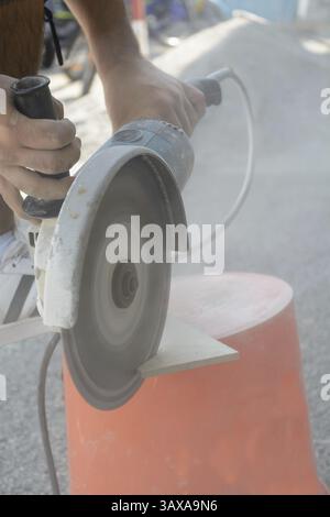 Skilled worker cuts tiles with angle grinder under dust exposure Stock Photo