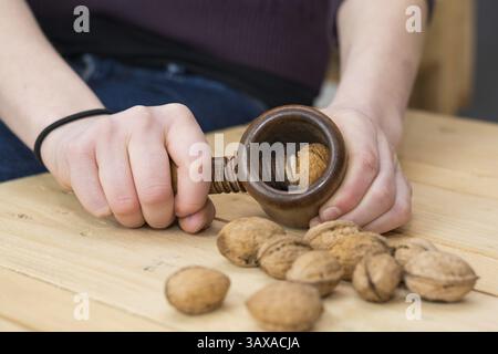 Person cracking walnuts on a rustic wooden table with a nostalgic nutcracker Stock Photo