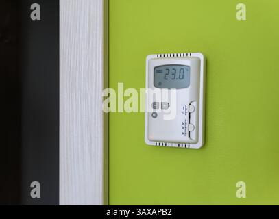 A wall-mounted climate control panel with a thermometer reading 23 degrees Celsius mounted on a bright green wall Stock Photo
