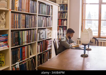 Perm, Russia - April 13, 2025: Young man reading a book in a library. Student studying in a library Stock Photo