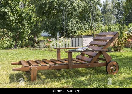 Garden lounger made of sustainable wood in a romantic garden with a book Stock Photo