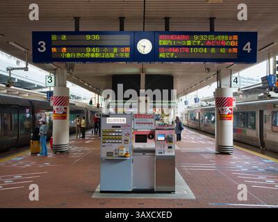 Passengers wait at Hakata Station in Fukuoka, Kyushu, Japan, with JR trains at platforms 3 and 4 beneath bilingual digital departure boards and vendin Stock Photo