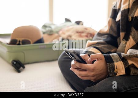 Hands holding phone with packed suitcase in background on bed Stock Photo