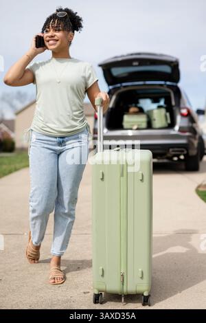 Smiling woman walks with suitcase while talking on phone Stock Photo