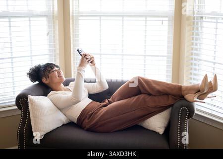Woman laying on back on couch texting on phone Stock Photo