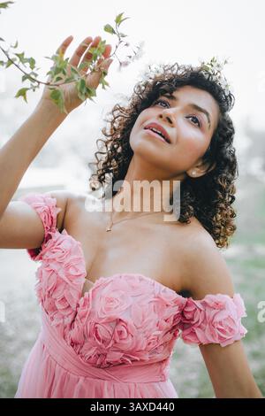 An Indian woman in a soft pink dress touches a cherry blossom branch Stock Photo