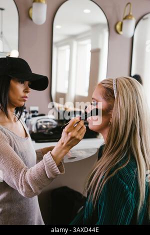 Cosmetologist brushes blush on blond woman in salon Stock Photo