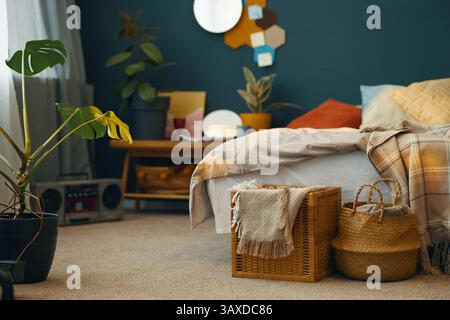 Warm and inviting bedroom featuring woven baskets, a cozy bed with blankets, assorted plants, geometric wall artwork, and soft natural light coming th Stock Photo
