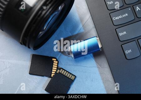 Flash drive connected to laptop, SD memory cards and camera lens on gray table, flat lay Stock Photo