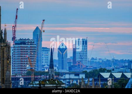 Modern buildings and construction cranes in the London skyline at dusk, with historic rooftops and spires in the foreground, United Kingdom. Stock Photo
