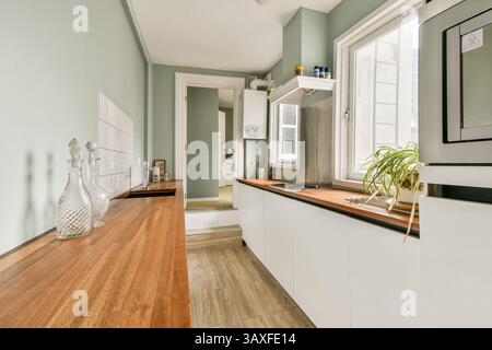 This modern kitchen features an elegant wooden countertop, minimalist design, and soft green walls, creating a cozy yet contemporary atmosphere for cooking. Stock Photo