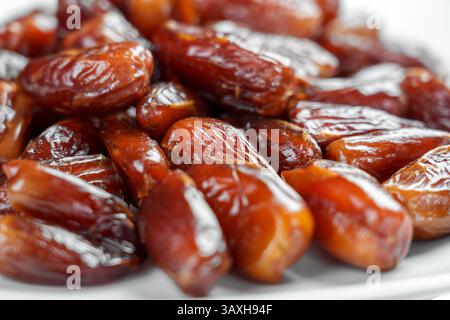 Dried dates in glass plate on white table. Macro shot. Front view Stock Photo