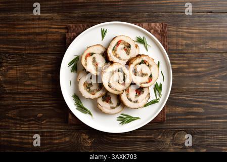 Sliced diet pork roll stuffed with mushroooms, dried tomatoes, spinach on white plate on brown wooden background. Top view, flat lay Stock Photo