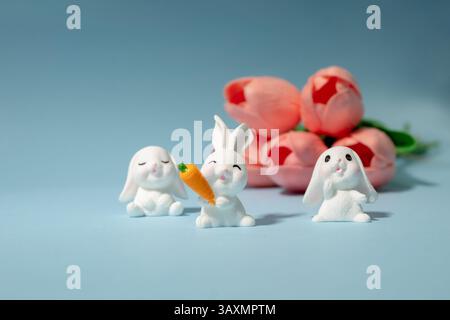 Miniature white bunnies with carrot and pink tulips with blue background. Easter spring concept. Stock Photo