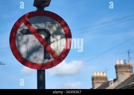 No left turn road sign with blue sky a chimneys &  TV antennas of terraced houses in the background in the street in Bury St Edmunds, Suffolk, UK Stock Photo