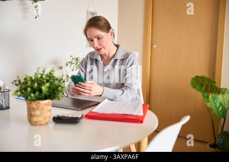 Focused freelancer using smartphone at home office desk Stock Photo