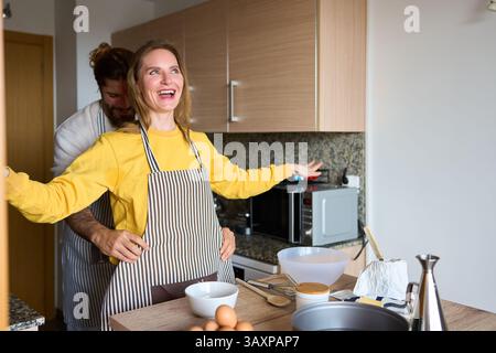 Happy couple wearing aprons baking together in modern kitchen Stock Photo