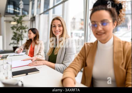 Portrait of confident businesswoman with note pad working with female coworkers in modern board room Stock Photo