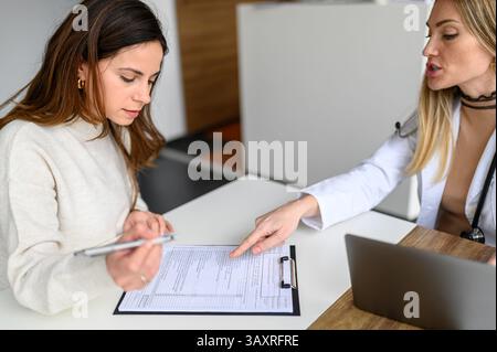High angle view of female doctor pointing at details while patient filling form on desk during consultation Stock Photo