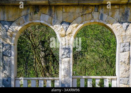 A beautiful stone archway frames vibrant greenery in a serene outdoor location. Natural light enhances the scene, showcasing the intricate textures of Stock Photo