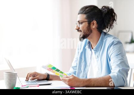 Young eastern interior designer holding color swatch samples and working on laptop Stock Photo