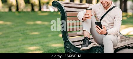 Young man enjoying coffee while using smartphone in urban park setting Stock Photo