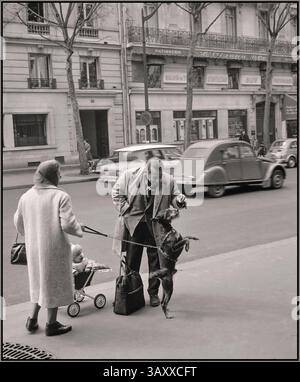 Paris 1965 reportage moment lifestyle fashion street reportage. Citroen Deaux Chevaux passing in background Van de Poll [Street life in Paris] Man playing and feeding the dog of a passer-by 1965  France, Paris Stock Photo