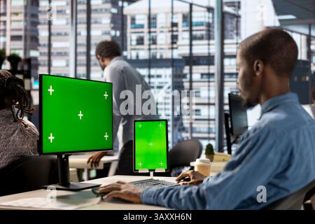 Businessman seated at workstation with green screen on devices, working on solving administrative tasks for enterprise growth. Developing performance metrics to support project goals. Stock Photo