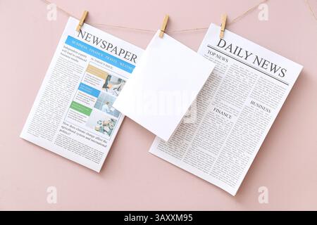 Newspapers and blank sheet of paper hanging on rope against pink background Stock Photo