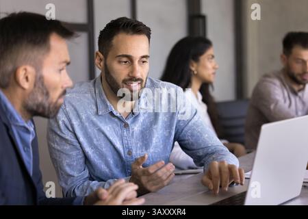 Two colleagues sit at desk working together using laptop Stock Photo