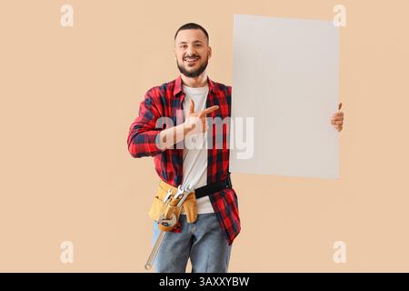 Happy male construction worker with professional wrenches pointing at blank poster on beige background Stock Photo