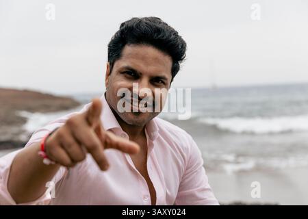 A smiling and confident Indian man pointing towards the camera while at the beach, photo with copy space. Stock Photo