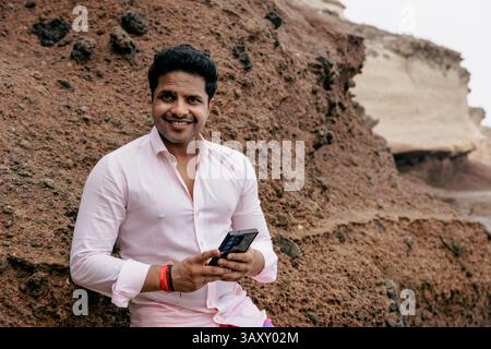 Portrait of a smiling man holding his smartphone and looking at the camera outdoors. Stock Photo