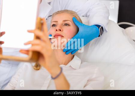 Cosmetologist applying marks on face of young female client Stock Photo